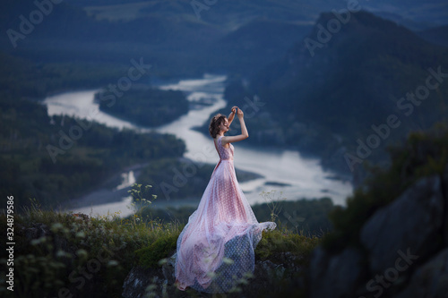 A girl in a pink dress with a long train is dancing on the top of the mountain