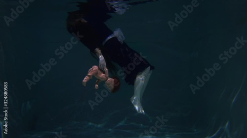 Beautiful and cute girl swims underwater in the pool with her doll. Disappointment and sadness. Long hair and blue dress. Water and the ocean. Fairy tale