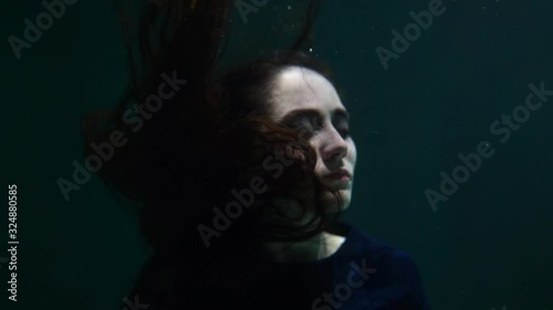 A brunette girl underwater looks at the camera and her hair develops. Mermaid and Nymph. Beautiful girl in the pool. Long hair.