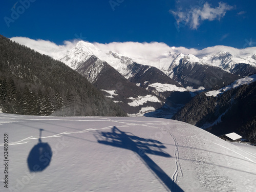 Cable car lift shadow silhouette on fresh snow with Aurina valley and mountains with foggy clouds on horizon below blue sky during sunny day in Speikboden ski resort in Italy photo