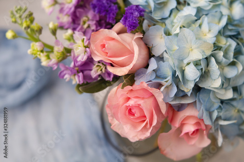 Top View Bouquet of Pink Roses  Blue Hydrangea  and Purple Flowers in a Clear Vase on Neutral Background with Blue Fabric in background