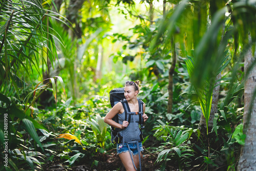 Slender young girl with a hiking backpack in the jungle. White Caucasian girl hiking in the jungle on sunset.