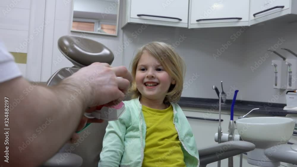 Dentist shows to a little cute girl a jaw model to explain how to brush her teeth Dentist shows to a little cute girl a jaw model to explain how to brush her teeth