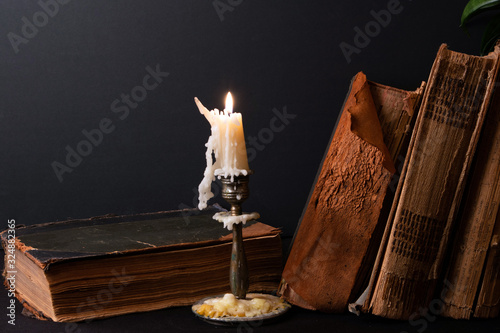 Stack of ancient books with yellowed shabby pages and candlestick with lighted candle 