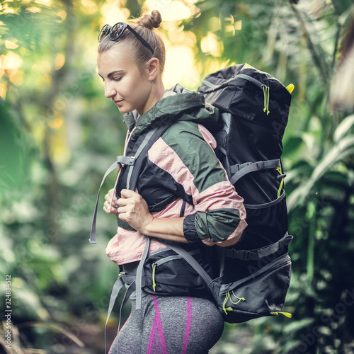 Portrait of a white caucasian girl with a hiking backpack. Young girl in a spring jacket and clothes for hiking on the background of the jungle.