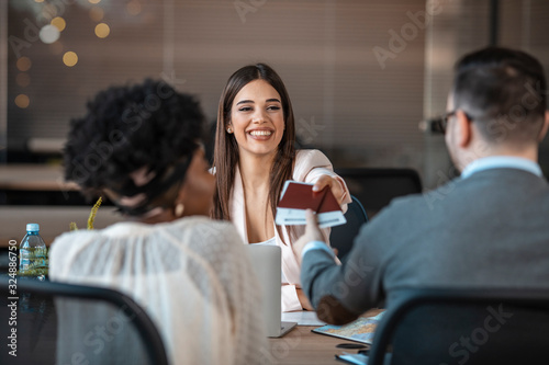 A young man and a woman came to the travel agency. They want to go on a trip during their holidays. Female travel agent giving tickets to young happy couple. photo