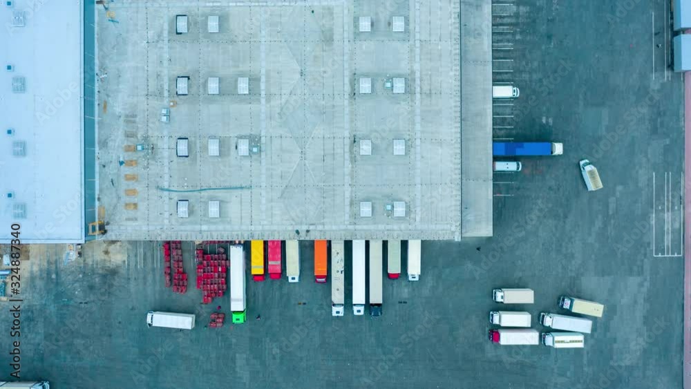 Aerial view of the large logistics park with warehouse, loading hub with semi trucks with cargo trailers standing at the ramps for load/unload goods at night. Hyper lapse - time lapse. Aerial view of the large logistics park with warehouse, loading hub with semi trucks with cargo trailers standing at the ramps for load/unload goods at night. Hyper lapse - time lapse.