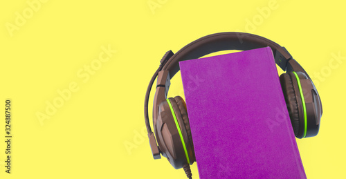 Audio book and e-learning concept. Headphones and purple book on yellow background. Listening to a book. Copyspace.