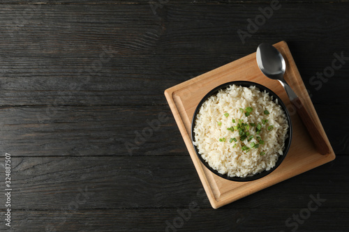 Board with bowl of delicious rice on wooden background, top view