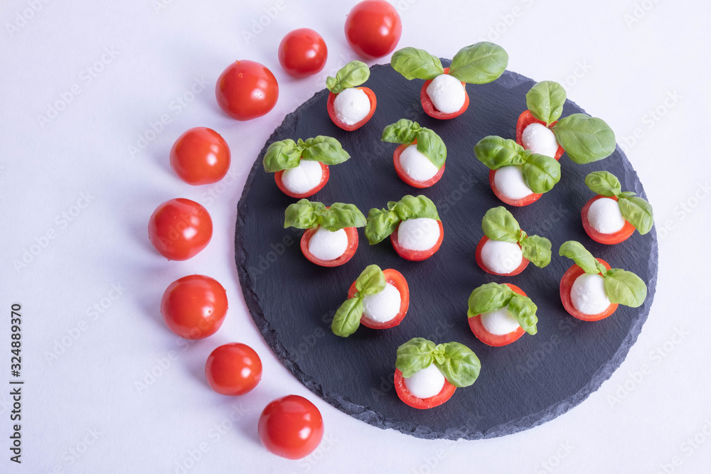 composition of basil, tomatoes and mozzarella on a stone black tile composition of basil, tomatoes and mozzarella on a stone black tile