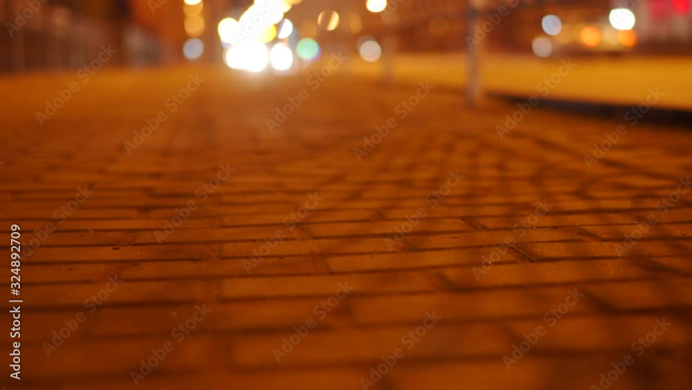 Night city street, surface level of dark stone tile sidewalk pavement and cars on the road. Night city street, surface level of dark stone tile sidewalk pavement and cars on the road.