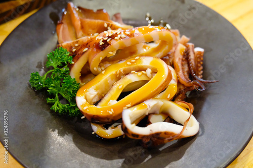 Grilled squid in soy sauce and topping with white sesames on a black plate in the Japanese restaurant, Chiangmai, Thailand.