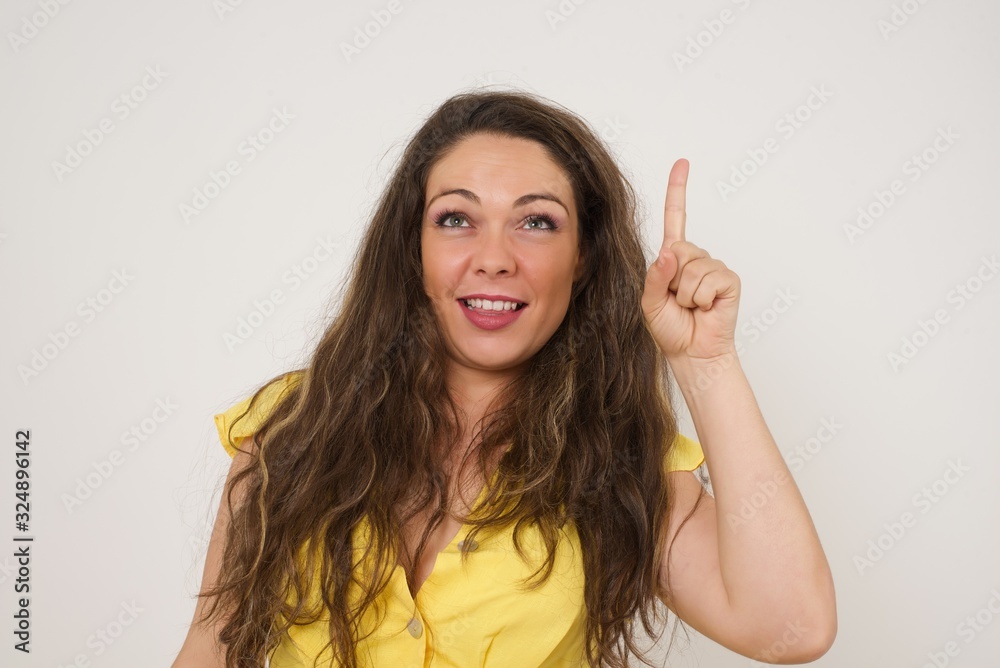 Close-up portrait of charming young blonde hipster woman in casual clothes pointing with one finger up, looking up and smiling, I have an idea, I know the answer or the solution. Close-up portrait of charming young blonde hipster woman in casual clothes pointing with one finger up, looking up and smiling, I have an idea, I know the answer or the solution.