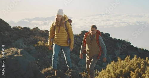 Young active couple hiking up a mountain above the clouds with backpacks, adventurous backpackers in the great outdoors photo
