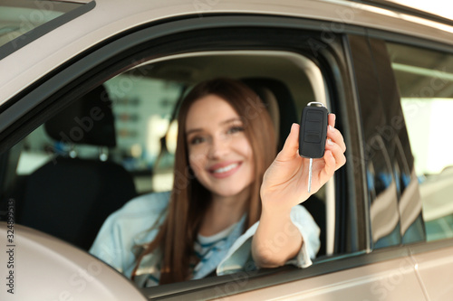 Beautiful woman sitting in modern car at dealership, focus on hand with key