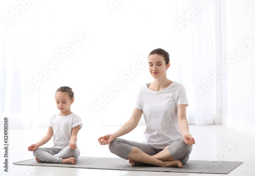 Young mother with little daughter practicing yoga at home