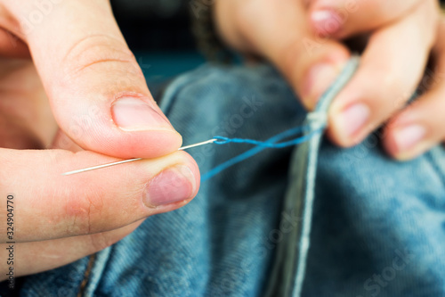 Girl sews jeans with a needle. The girl's hands holding a needle for sewing.