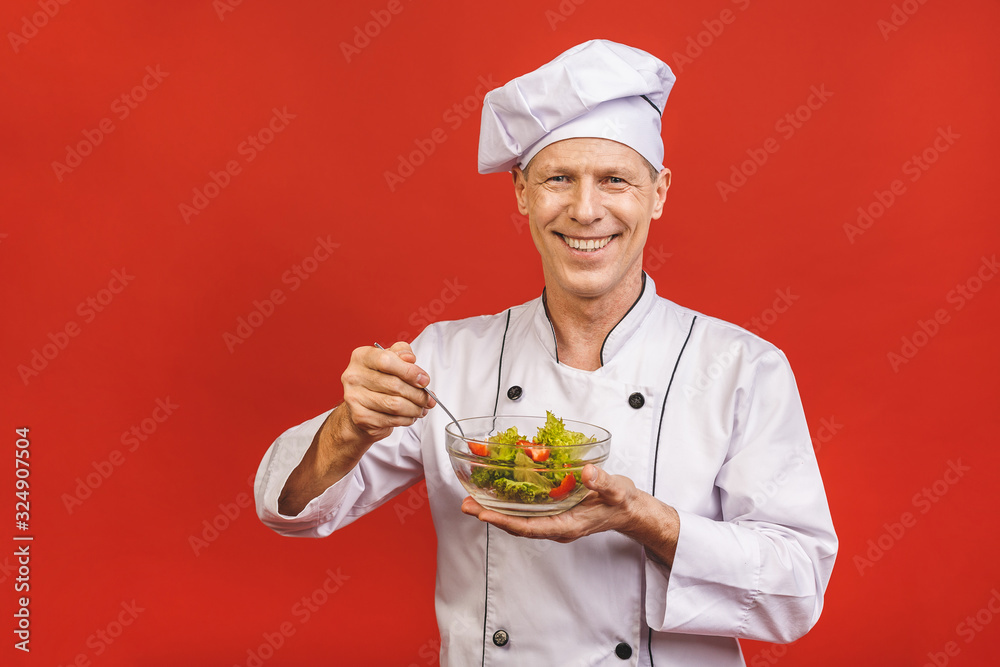 Picture of happy young senior chief cook in uniform standing isolated over red wall background, holding salad. Picture of happy young senior chief cook in uniform standing isolated over red wall background, holding salad.