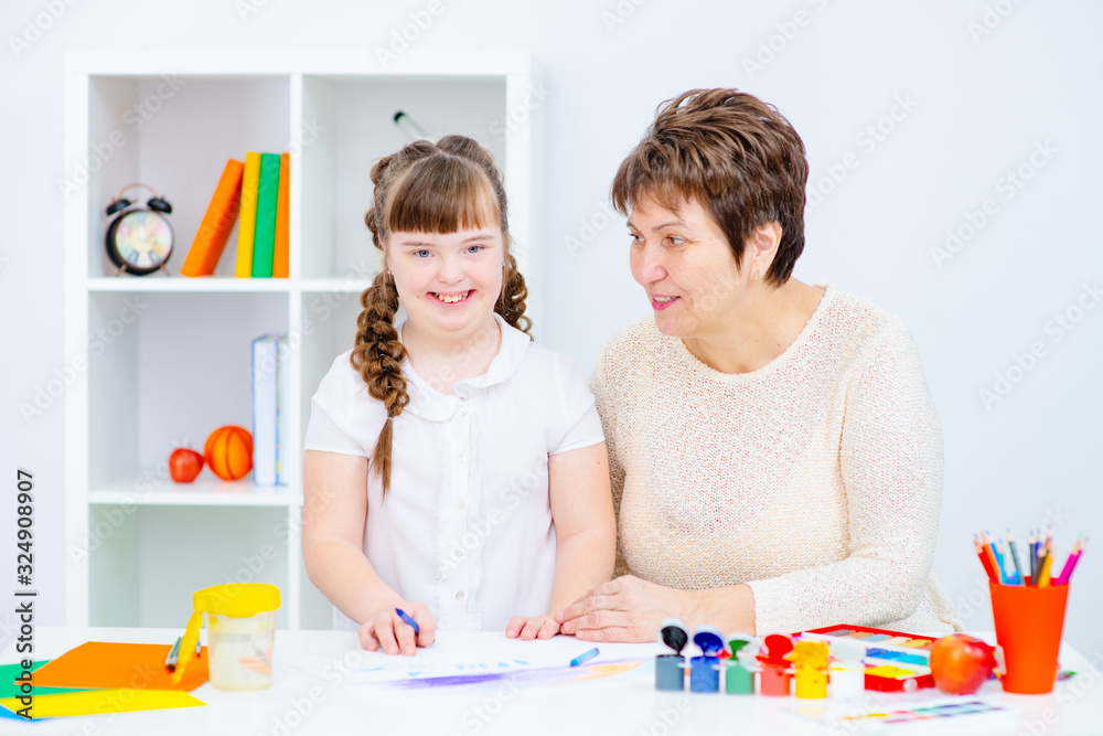 Fototapeta premium Girl with Down Syndrome works with her teacher at home