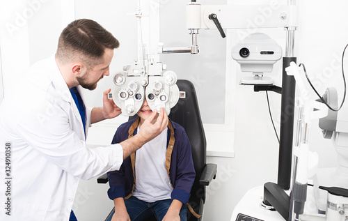 Fotografia Male optometrist checking teenage boy eye health and visual acuity