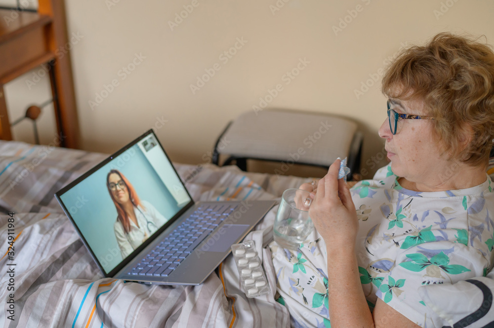 An elderly woman is talking with a doctor on Skype. A pensioner suffers from a respiratory disease and blows her nose. Online consultation. An elderly woman is talking with a doctor on Skype. A pensioner suffers from a respiratory disease and blows her nose. Online consultation.