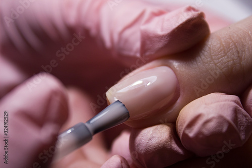 The manicurist applies a layer of gel Polish to the client's nail. Applying pink nail Polish with a brush. Coating the nail plate with nail Polish. Professional manicure in the salon close-up.