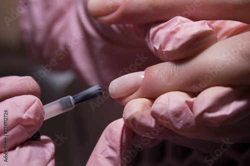 The manicurist applies a layer of gel Polish to the client's nail. Applying pink nail Polish with a brush. Coating the nail plate with nail Polish. Professional manicure in the salon close-up.
