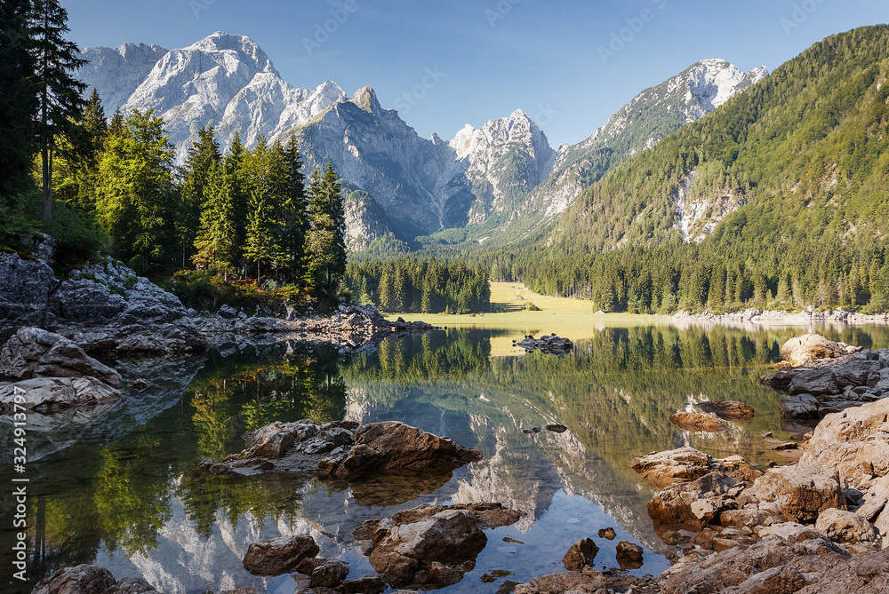 Scenic image of fairy-tale Mountain lake under sunlit. Amazing Nature Landscape. Wonderful sunny morning. Beautiful scenery of the majestic Fusine lakeside in Julian Alps. Perfect natural background