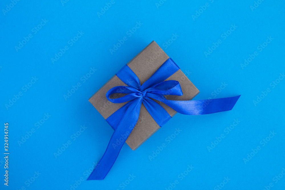 Gift with blue bow in the center of  the blue background. Top view. Copy space.