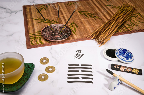 Close up of an I Ching arrangement with coins, a hexagram written with an ink brush on rice paper, yarrow stalks and a cup of tea.