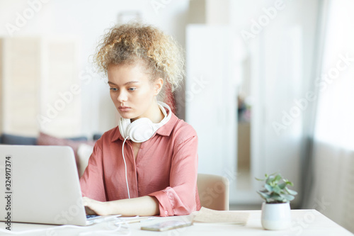 Serious young woman sitting at her workplace and typing on laptop computer at office