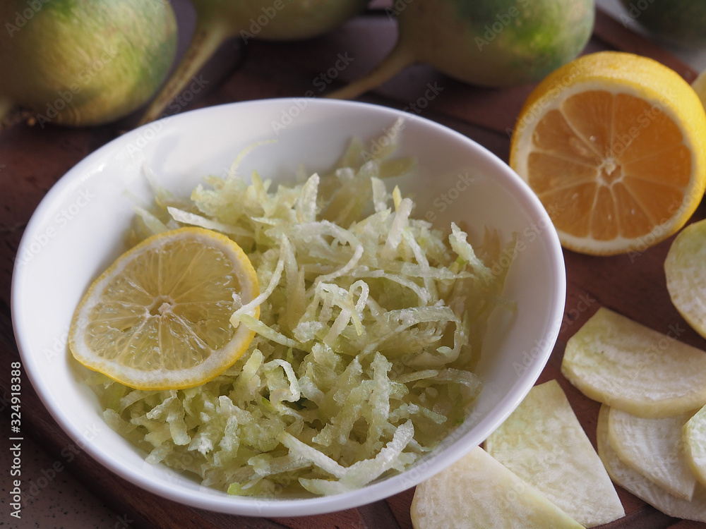 Salad of raw grated green radish and lemon in a white bowl, vegetables, pieces of radish on a wooden stand closeup. Recipe for a vegetarian dish for proper nutrition. Salad of raw grated green radish and lemon in a white bowl, vegetables, pieces of radish on a wooden stand closeup. Recipe for a vegetarian dish for proper nutrition.