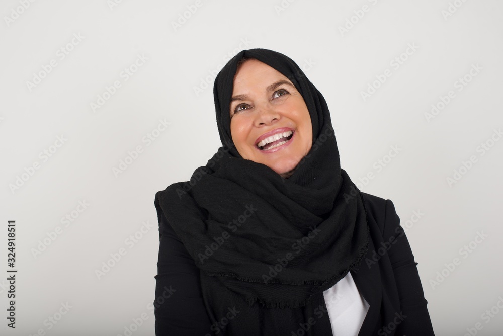 Beautiful smiling brunette female with broad smile, shows white teeth, wears casual t shirt, stands over gray studio wall rejoices having day off. Woman standing indoors. Beautiful smiling brunette female with broad smile, shows white teeth, wears casual t shirt, stands over gray studio wall rejoices having day off. Woman standing indoors.