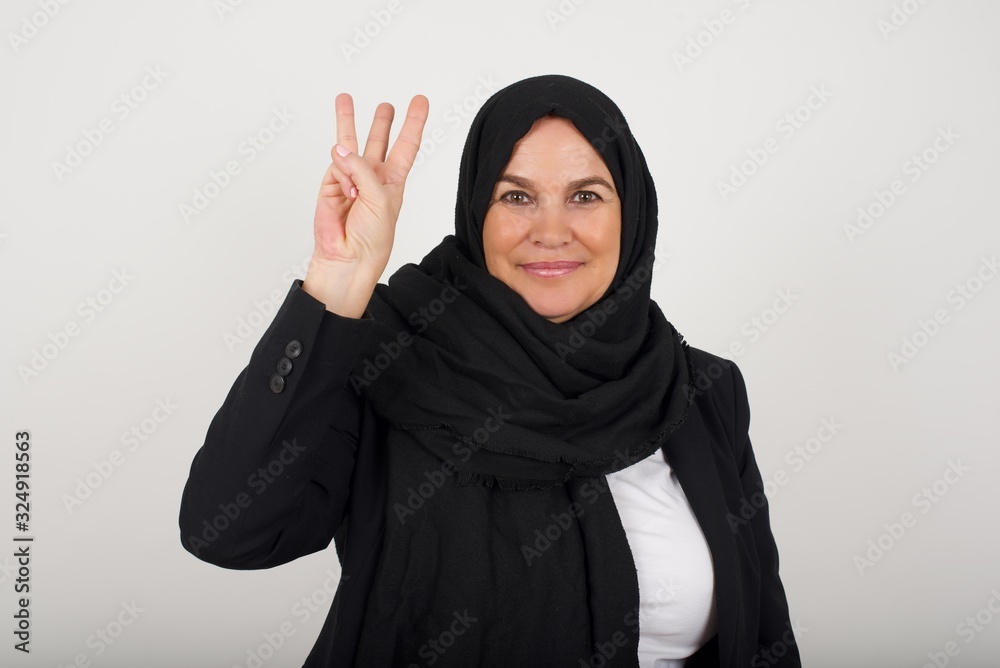 Young blonde woman standing standing against gray wall showing and pointing up with fingers number three while smiling confident and happy. Young blonde woman standing standing against gray wall showing and pointing up with fingers number three while smiling confident and happy.