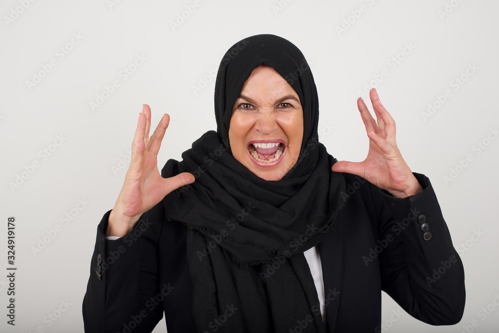 Screaming, hate, rage. Crying emotional angry muslim woman screaming on blue studio background. Emotional, young face. Female half-length portrait. Human emotions, facial expression concept. Screaming, hate, rage. Crying emotional angry muslim woman screaming on blue studio background. Emotional, young face. Female half-length portrait. Human emotions, facial expression concept.