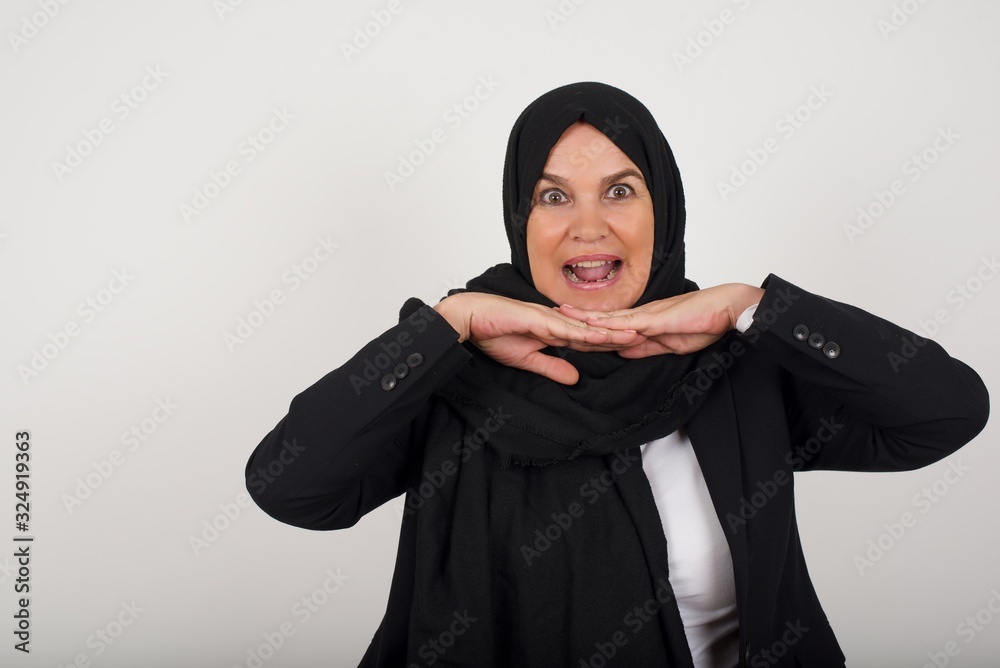 Pretty surprised muslim fooling around in studio and jumping. Adorable woman wearing black clothes dancing on colorful background and touching chin with hands Pretty surprised muslim fooling around in studio and jumping. Adorable woman wearing black clothes dancing on colorful background and touching chin with hands