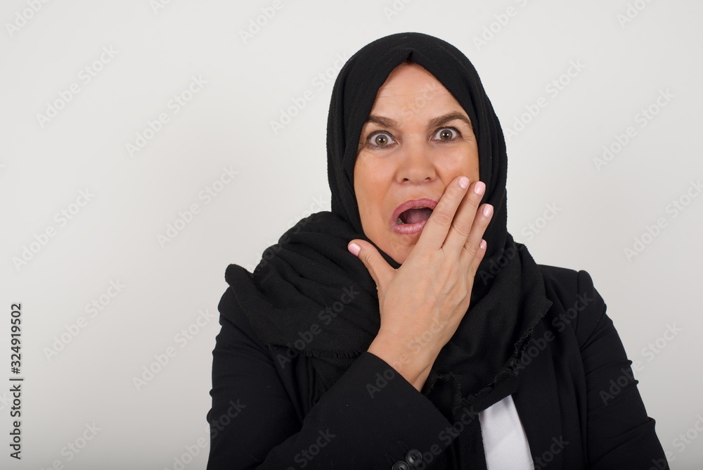 Anxiety - a conceptual image of a beautiful muslim caucasian woman covering her mouth with her hands and standing indoors. Scared from something or someone bitting nails Anxiety - a conceptual image of a beautiful muslim caucasian woman covering her mouth with her hands and standing indoors. Scared from something or someone bitting nails