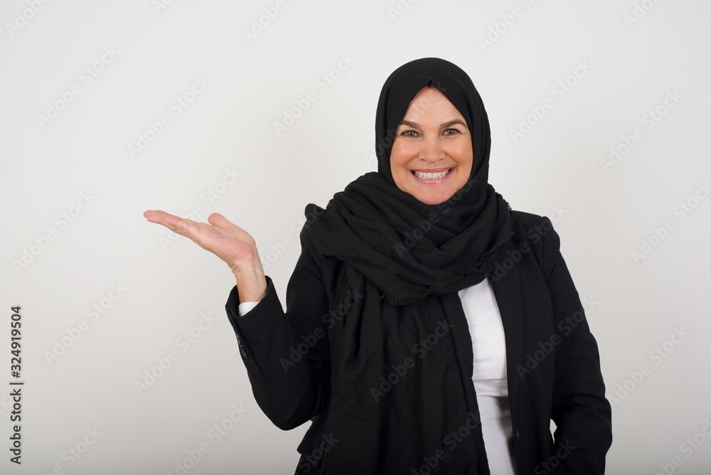 Positive glad muslim female says: wow how exciting it is, has amazed expression, shows something on blank space with open hand over isolated background. Advertisement concept. Positive glad muslim female says: wow how exciting it is, has amazed expression, shows something on blank space with open hand over isolated background. Advertisement concept.