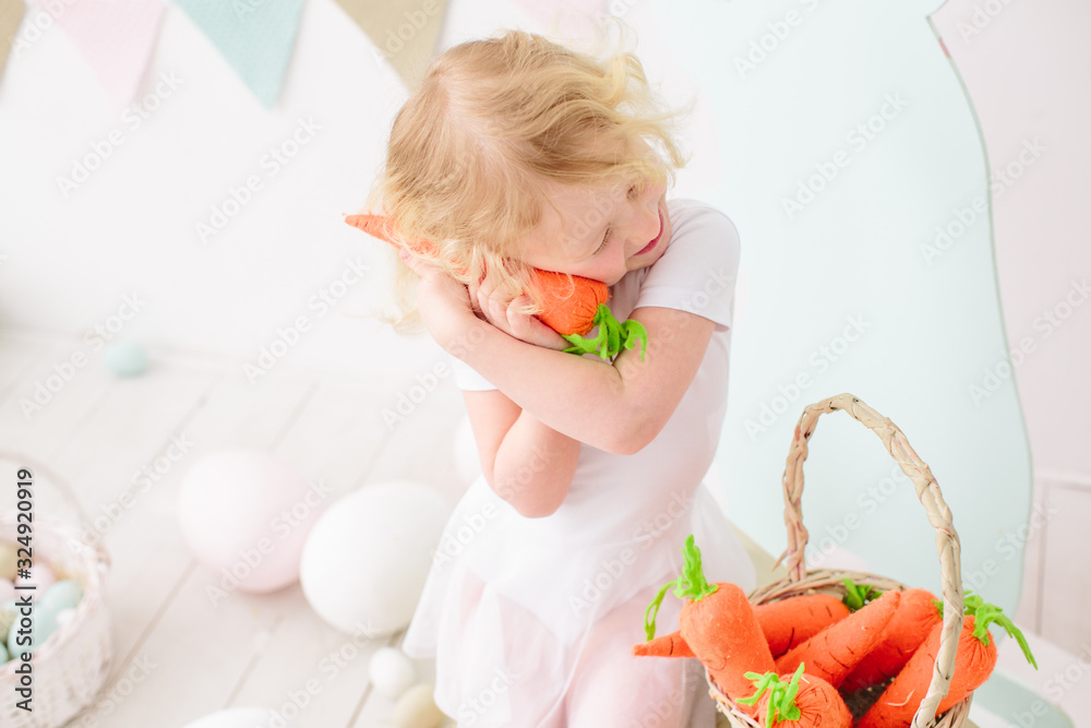 Fototapeta premium Blond girl playing and smile in kid room with easter decoration carrot toy 