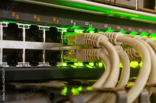 Telecommunication equipment is in the server room of the data center. Many Internet wires are connected to the main router. Gray cables are included in the network interfaces with a green indication.