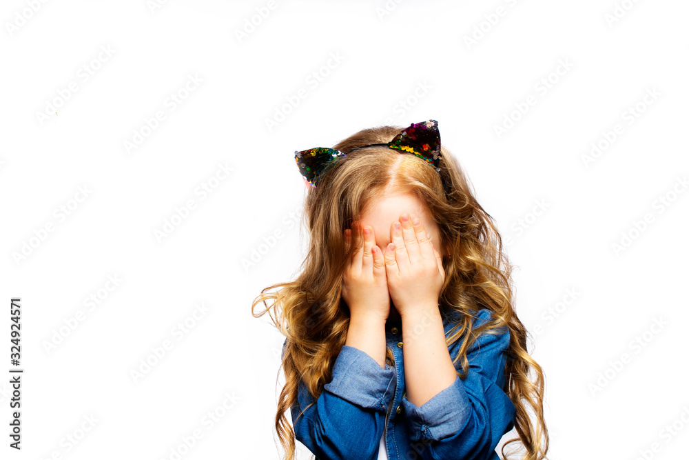Photo of a child on a white background with his eyes closed. The girl covers her face with her hands. The baby is hiding. Photo of a child on a white background with his eyes closed. The girl covers her face with her hands. The baby is hiding.