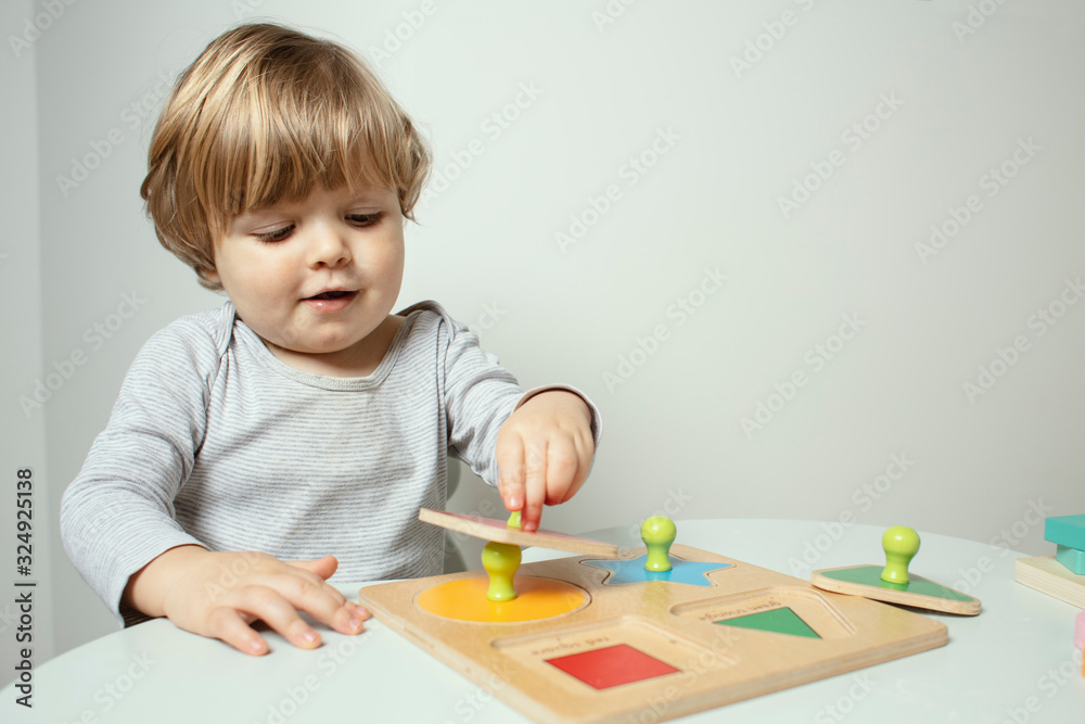 Beautiful toddler play with a wooden frame puzzle geometric figure toys at home. Toddler play with a color educational toy. Child play at the table in the baby room. Child development. Funny baby. Beautiful toddler play with a wooden frame puzzle geometric figure toys at home. Toddler play with a color educational toy. Child play at the table in the baby room. Child development. Funny baby.