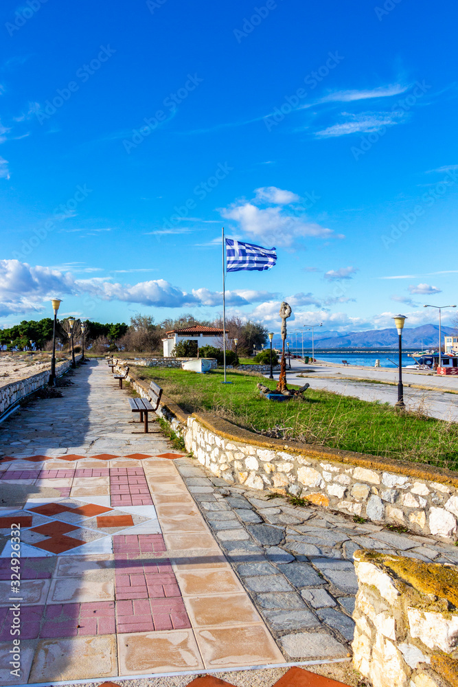 Empty November off-season promenade with the Greek flag. The port of Fanari, Rhodope prefecture, Greece to the right