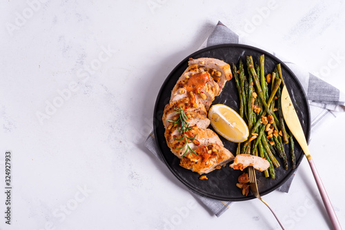 grilled chicken breast fillet with asparagus and lemon in slate plate and white stone background