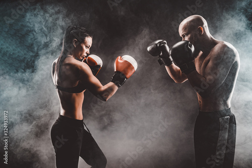 Shirtless Woman exercising with trainer at boxing and self defense lesson, studio, smoke on background. Female and male fight,