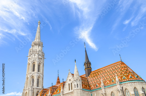 The spire of the famous Matthias Church in Budapest  Hungary. Roman Catholic church built in the Gothic style. Orange colored tile roof. Blue sky and white clouds above. Horizontal photo