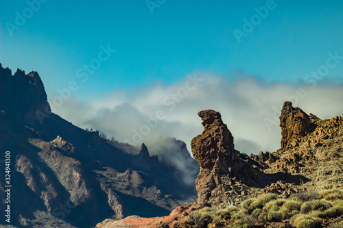 Mountains and lava fields around volcano Teide, partly covered by the clouds. Bright blue sky. Teide National Park, Tenerife, Canary Islands, Spain