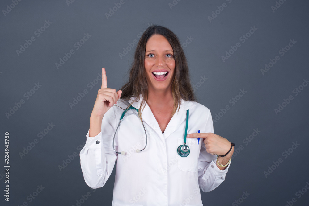Positive glad doctor female wearing medical uniform and a stethoscope says: wow how exciting it is, has amazed expression, indicates something. One hand on her chest and pointing with other hand. Positive glad doctor female wearing medical uniform and a stethoscope says: wow how exciting it is, has amazed expression, indicates something. One hand on her chest and pointing with other hand.
