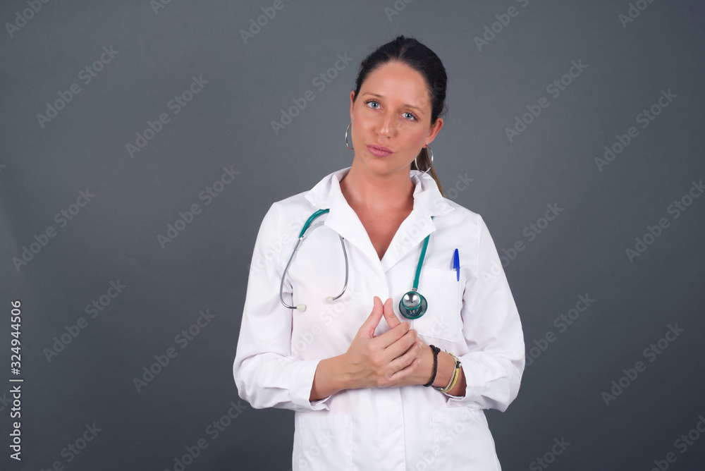 Business Concept - Portrait beautiful doctor woman holding hands with confident face isolated over gray Background. Business Concept - Portrait beautiful doctor woman holding hands with confident face isolated over gray Background.