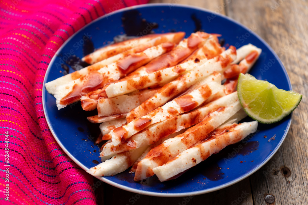 Mexican jicama cutted with chili powder and piquant sauce on wooden background Mexican jicama cutted with chili powder and piquant sauce on wooden background